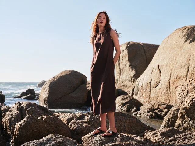 Woman wearing a floral print linen dress styled with a stone coloured linen blazer and chunky cream sandals.