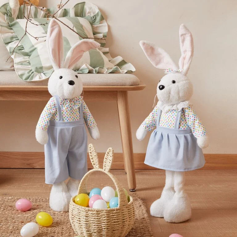 Wooden tray on a bed. On the tray are two cups of tea in bunny Easter themed mugs and a bunny Easter basket filled with eggs.
